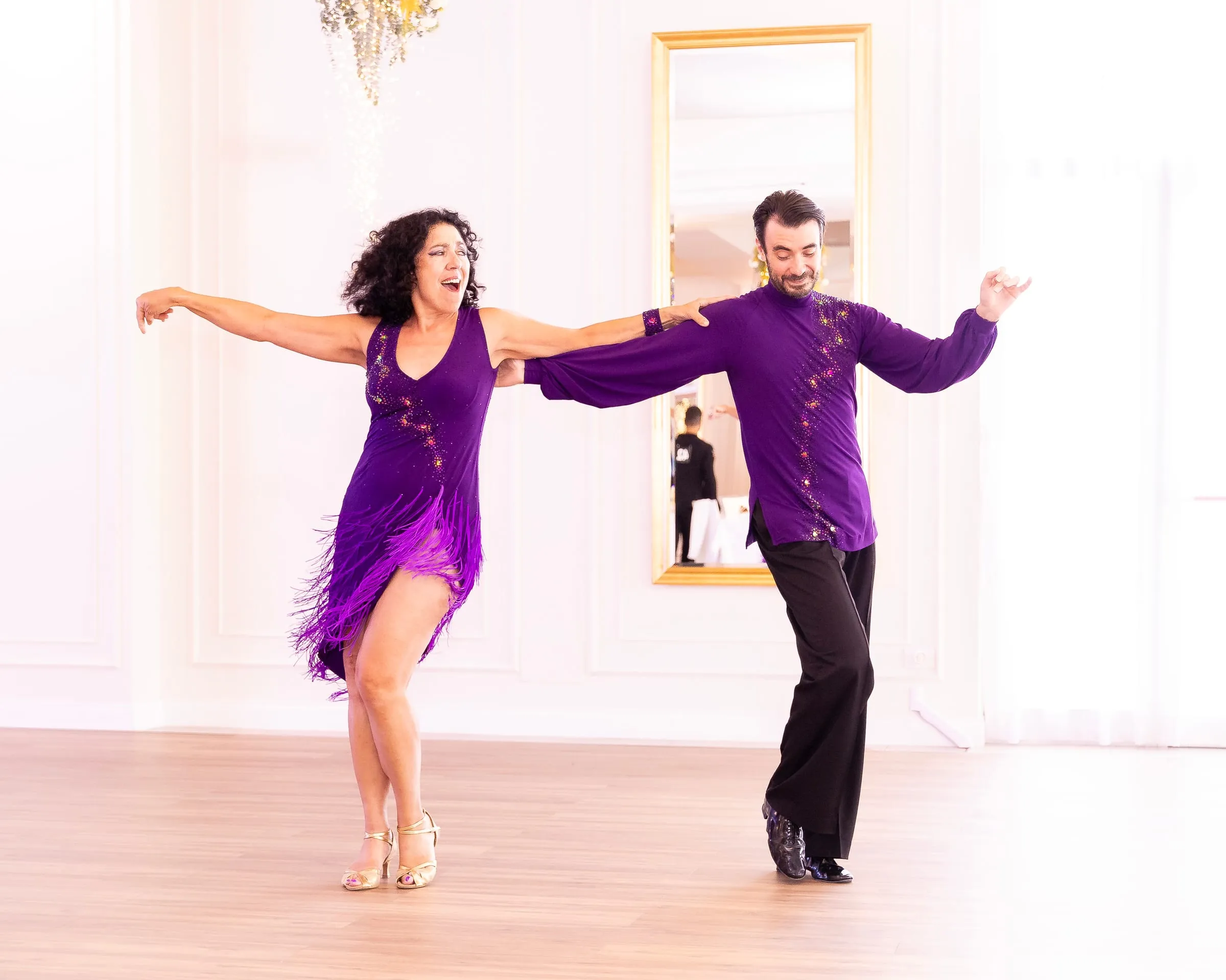 Tanzpaar in violetten Kostümen springt mit weit geöffneten Armen durch eine Swing-Figur.